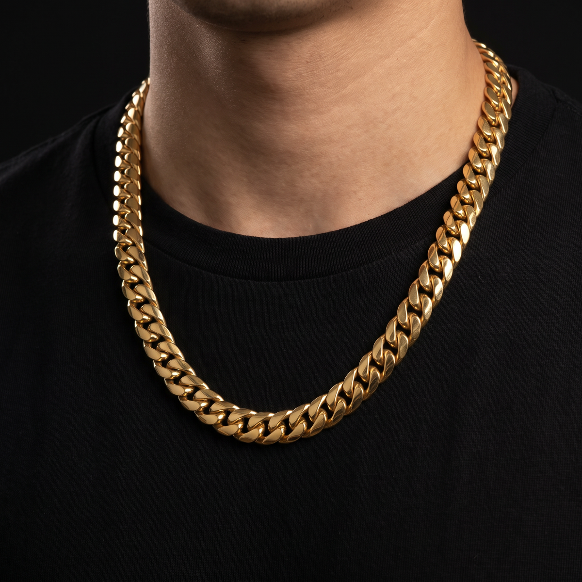 Person wearing a solid gold Miami Cuban link chain over a black tee, on a black background