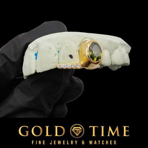 Gold 2 piece grill with a green oval gem canine and moissanite tip held on a dental mold, Gold Time