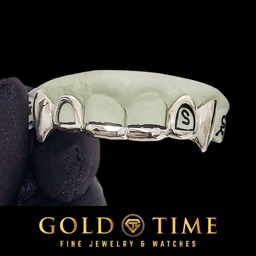 A silver fang grillz held by a black gloved hand against a black background, with the Gold Time logo at the bottom.