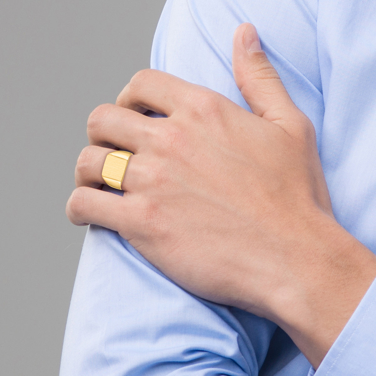 Hand wearing a gold ring with a blurred gray background