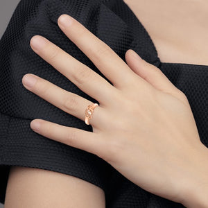 Rose gold cursive initial ring worn on the ring finger, hand resting on a dark sweater