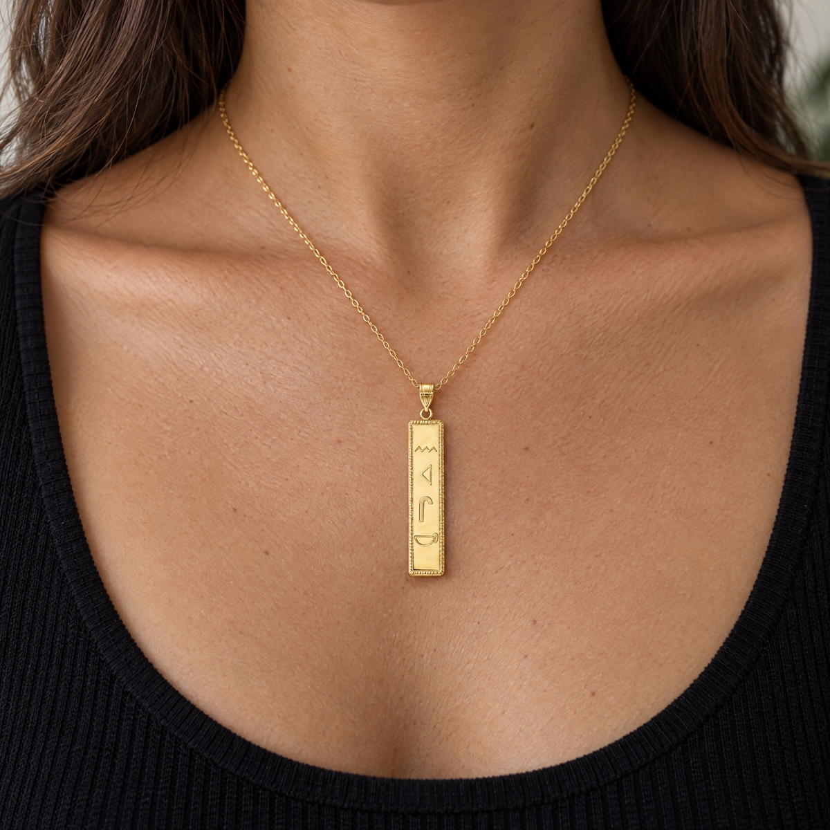 Yellow gold hieroglyphics cartouche bar pendant worn on a fine chain by a woman, lifestyle photo, Gold Time