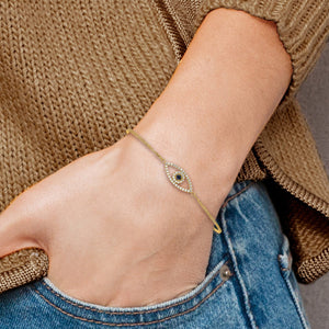 Yellow gold evil eye bracelet worn on a wrist with a sweater and jeans