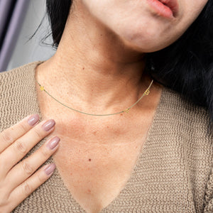 Woman wearing a dainty gold necklace with small initials and symbols spaced along the chain