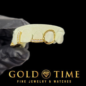 Side view of yellow gold grillz with an open face canine and a moissanite lateral tip bar on a dental mold held in a gloved hand, Gold Time
