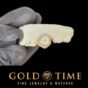 Gloved hand holding a mold with an iced open face fang cap on the canine and an iced tip bar on the neighboring tooth, Gold Time logo