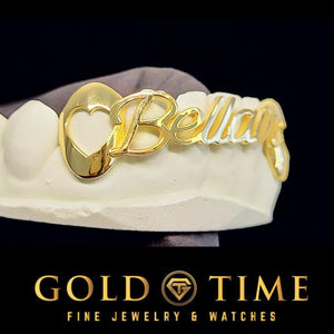 Close-up of a gold open heart cut-out canine and the start of a cursive name on a nameplate grill