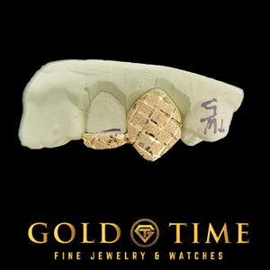 Close-up of a gold fang cap with a trillion diamond-cut pattern on a dental mold