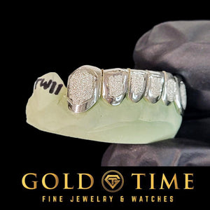 Gloved hand holding white diamond dust box grillz with perm cuts