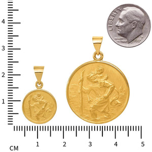 Small and large Saint Christopher medals on a ruler next to a dime