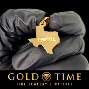 Gloved hand holding a gold Texas state pendant engraved with the word HOME and a small heart