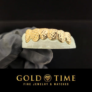 Yellow gold box trillion diamond cut grillz on a dental model, each tooth framed with a cut face