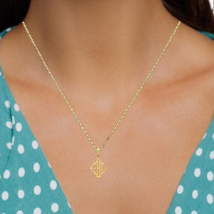 Woman in a teal polka dot top wearing the yellow gold monogram pendant on a fine cable chain