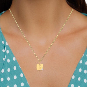 Woman wearing the dainty yellow gold cushion initial charm on a fine chain