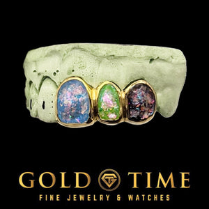 Three gold framed grillz caps with blue, green and purple galaxy enamel faces on a dental mold