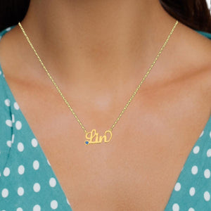 Woman wearing a gold script birthstone name necklace with a teal polka dot top