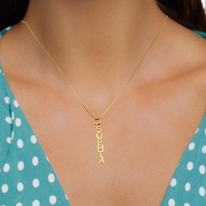 Vertical gold name plate charm worn on a chain at the neckline