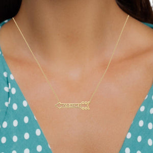 Model wearing a dainty gold arrow name necklace over a teal polka dot top