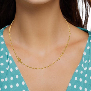 Woman wearing a 14K gold rosary necklace with a polka dot top