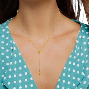 Woman wearing a gold plated beaded rosary necklace with a polka dot top