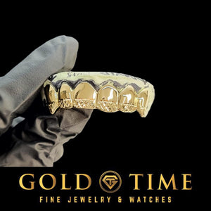 Yellow gold six piece grillz with trillion cut tips and canine fangs, held in a gloved hand