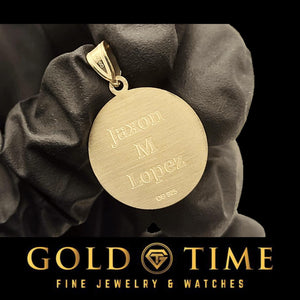 Satin-finish back of a gold baseball pendant engraved with a three-line name, held in a black gloved hand