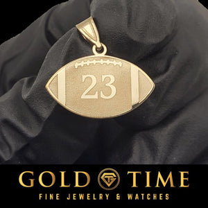 Gold football pendant with engraved jersey number 23 and laces detail, held in a black gloved hand