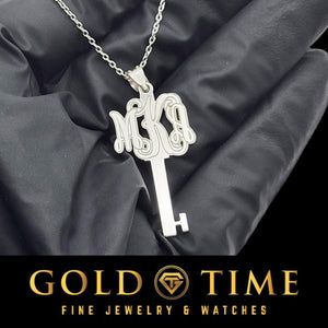 White gold monogram key pendant on its chain, held on a gloved hand