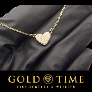 Yellow gold heart initial pendant on a cable chain held on a gloved hand