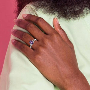 Hand on a mint green sleeve wearing a 14k white gold ring with a purple emerald-cut stone