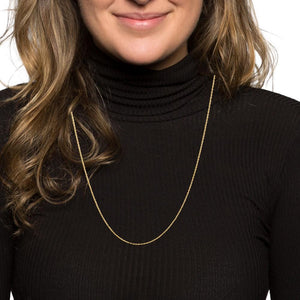 Woman wearing a thin yellow gold rope chain over a black turtleneck
