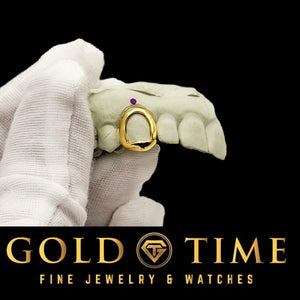 Single yellow gold open face cap grill on a dental mold held in a white-gloved hand