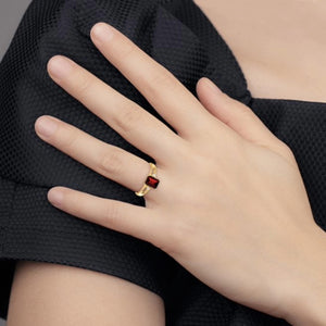 Hand resting on a black sleeve wearing a 14k yellow gold ring with a red emerald-cut garnet