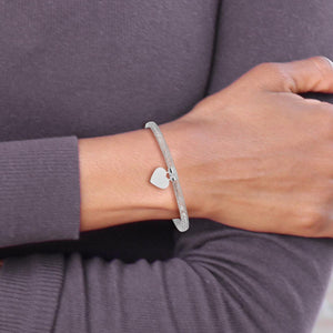 Wrist wearing the white gold mesh heart bangle with a gray top