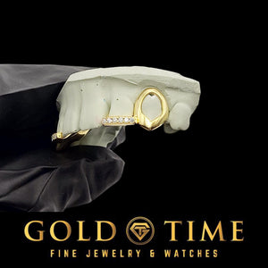 Gold open face canine and moissanite incisor tip grill on a dental mold held in a black gloved hand