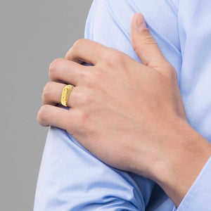 Hand wearing a gold ring with a blurred gray background