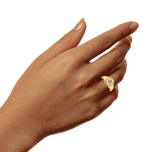 Hand wearing a small yellow gold diamond initial signet ring on the ring finger