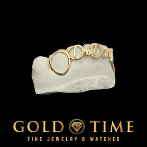 Side view of yellow gold name grillz showing the open face canine ring next to the script nameplate