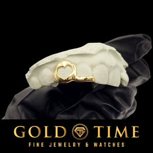 Yellow gold double cap grill with an open heart cut-out canine and a solid tip, on a white mold held in a black glove