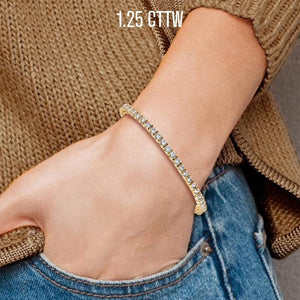 Wrist wearing a 1.25 cttw yellow gold diamond tennis bracelet with jeans