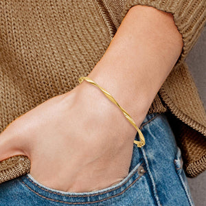 Wrist wearing a yellow gold twisted hinged bangle with a knit sweater and jeans