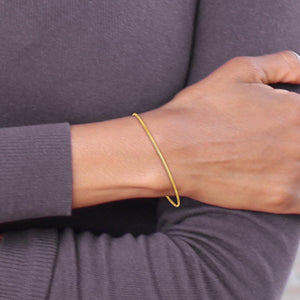 Wrist wearing a thin polished yellow gold bangle with a gray top