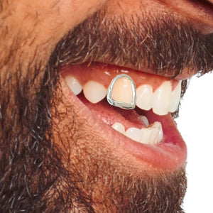 Close-up of a smiling bearded man wearing a white gold open face cap on one front tooth