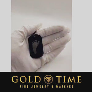 Video of a gloved hand holding the black dog tag engraved with a baby footprint